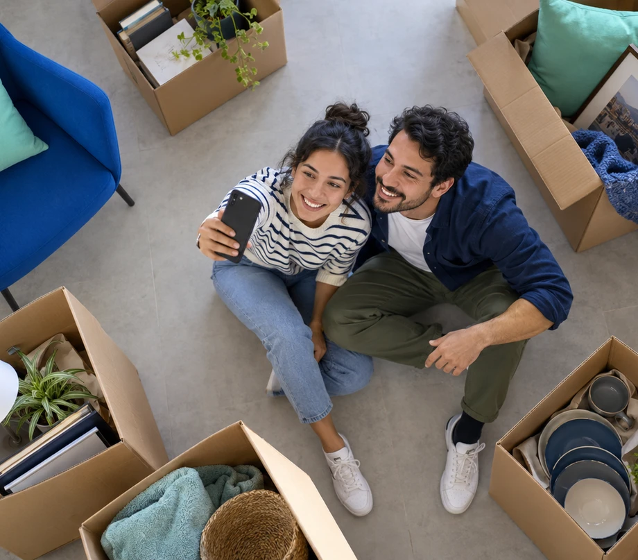 Pareja se toma una foto con su celular rodeada de cajas de mudanza